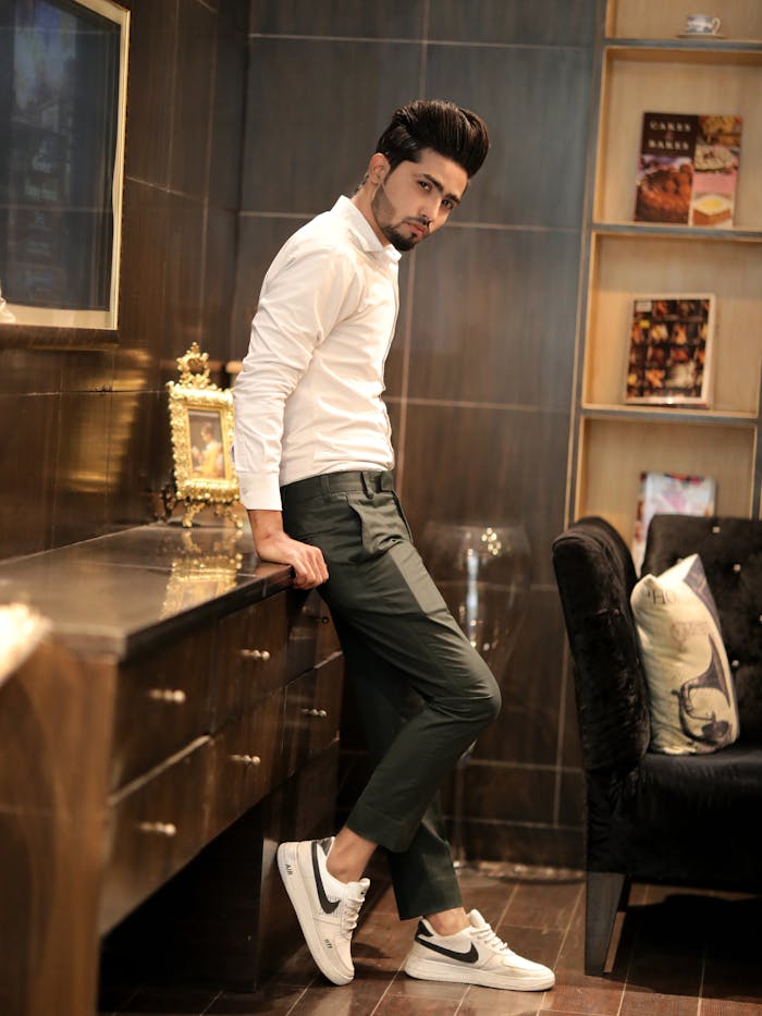 pexels photo 14564847 A fashionable man in white shirt and trousers leaning on a cabinet indoors.